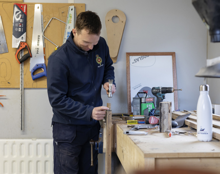 A maintenance team member holding a hammer, working on refurbishing a wooden ladder. 