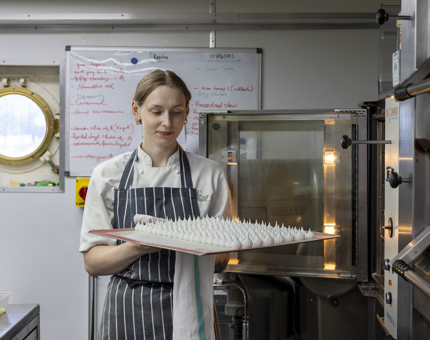 A chef in Britannia's Galley is removing a tray of small meringues from the oven. 