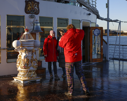 A man in a red jacket is taking a photo of two people on Britannia's Verandah Deck in the Port of Leith. 