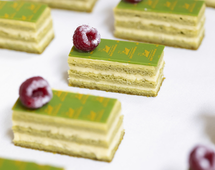 A close-up of green matcha cakes on a white tray, they are all adorned with a raspberry and a gold stencil on Britannia. 