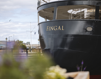 The back of Fingal Hotel. The ship has it's name, 'Fingal' written in gold letters. There is a herb garden in the foreground. 