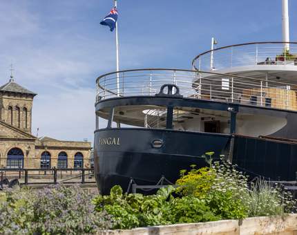 The back of Fingal. There is a herb garden in the foreground and a brick building in the background.
