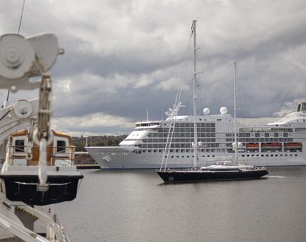 From Britannia's deck you can see a cruise ship docked in the port. A yacht is sailing past it.