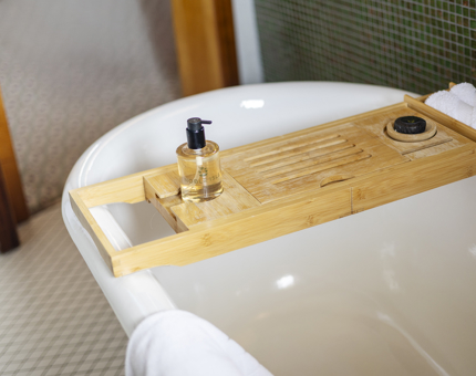 A bath tub with a wooden bath tray. 