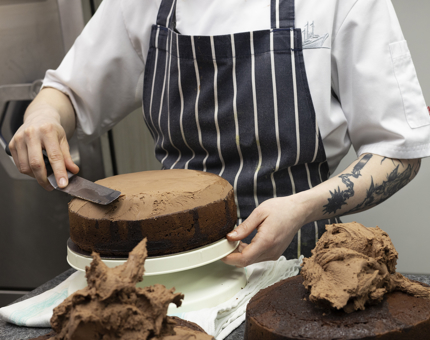 A close up of a chef icing a chocolate cake with chocolate icing. 