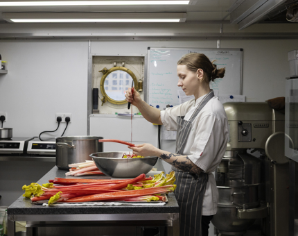 A Chef standing at a bench in a Galley preparing rhubarb. 
