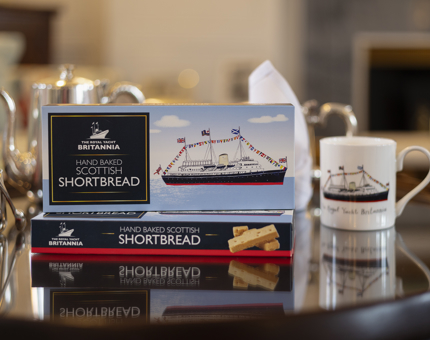 Two boxes of shortbread and a mug with an image of Britannia on it on a black table. 