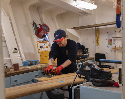 A Maintenance man is holding an electric sander, sanding wooden handrails. 