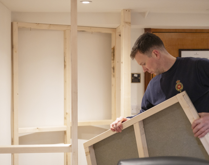 A maintenance man is aboard Fingal Hotel in Leith, he is creating storage in an onboard office. 