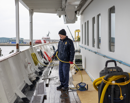 A Maintenance man on the deck of Britannia holding a hose washing it down.