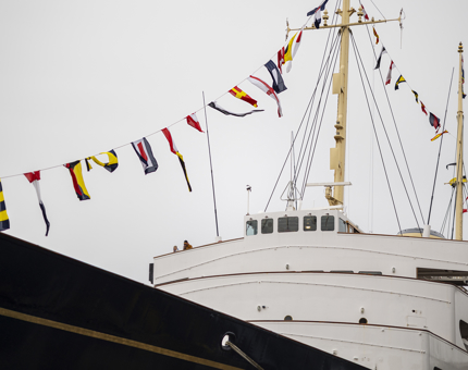 A view of the front of Britannia from the ground. There are colourful flags flying over the ship.