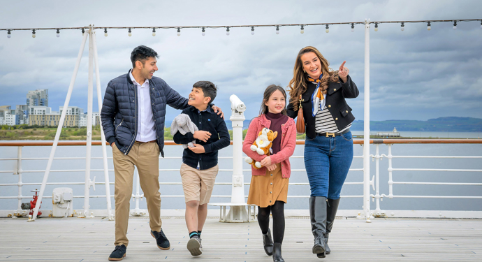 A family of four are on the deck of Britannia, the children are holding plush toys.