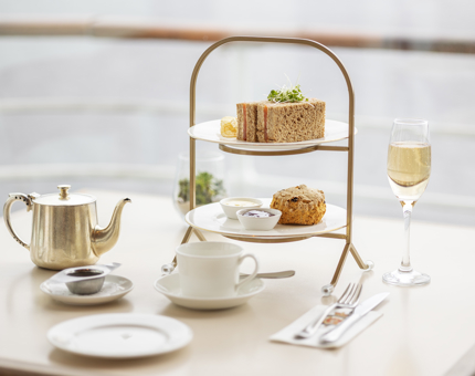 A table set with a cake stand, glass of fizz and pot of tea.