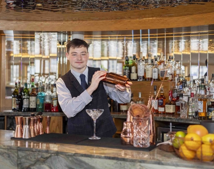 A bar man in Fingal's Lighthouse Restaurant shaking a cocktail shaker behind the bar. 