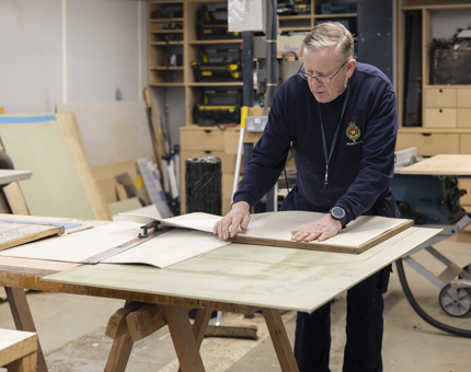 A maintenance team member is at a work bench, adding new tread to a step. 