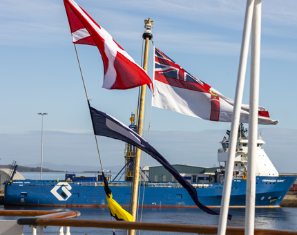 Flags are flying on the Verandah Deck and there is a large blue and white ship in the background. 