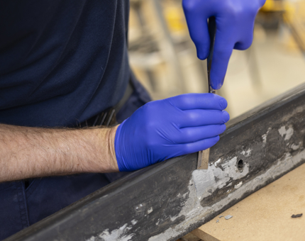 A close up of hands wearing blue gloves holding a chisel. 