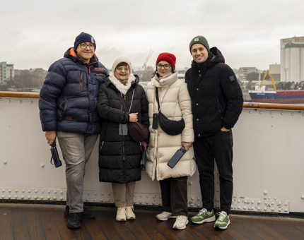 Four visitors posing for a photo on The Royal Yacht Britannia's Bridge. The Port of Leith is in the background. 