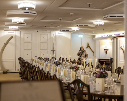 In the State Dining Room aboard Britannia a visitor is is listening to their audio guide handset. 