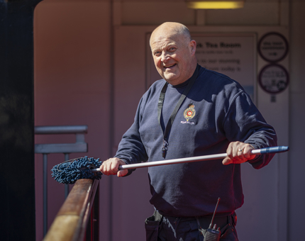 A Facilities Officer holding a duster, wiping down the railing outside the Engine Room. 