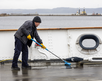 A maintenance team member on the deck scrubbing it with a brush. 