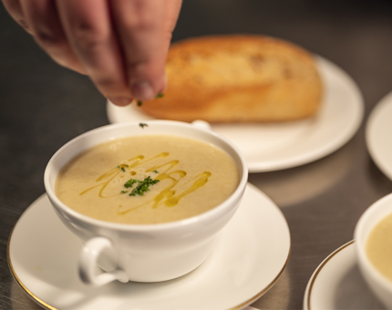 A hand sprinkling garnish onto a bowl of soup.