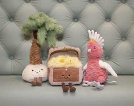 Three Jellycat plush toys. A treasure chest, palm tree and pink parrot.