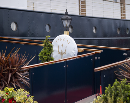 The entrance to Fingal Hotel, there is a walkway with plants and a perry buoy. 