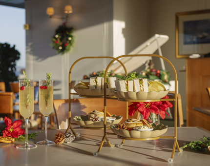 In the Tearoom aboard Britannia there are two stands containing cream teas and two mimosa cocktails. The sun is shining onto the table. 
