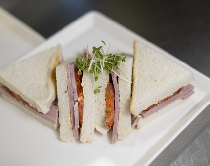 A ham and tomato sandwich on white bread on a white square plate. 