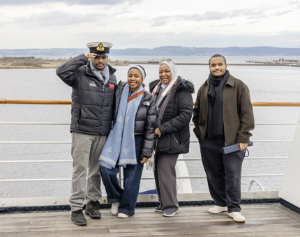 Four people posing for a photo on The Royal Yacht Britannia's Bridge. 