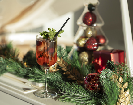 A glass of Festive Spritz sitting next to festive foliage in the Royal Deck Tearoom. 