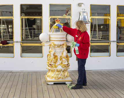 A woman polishing an ornate compass binnacle. 