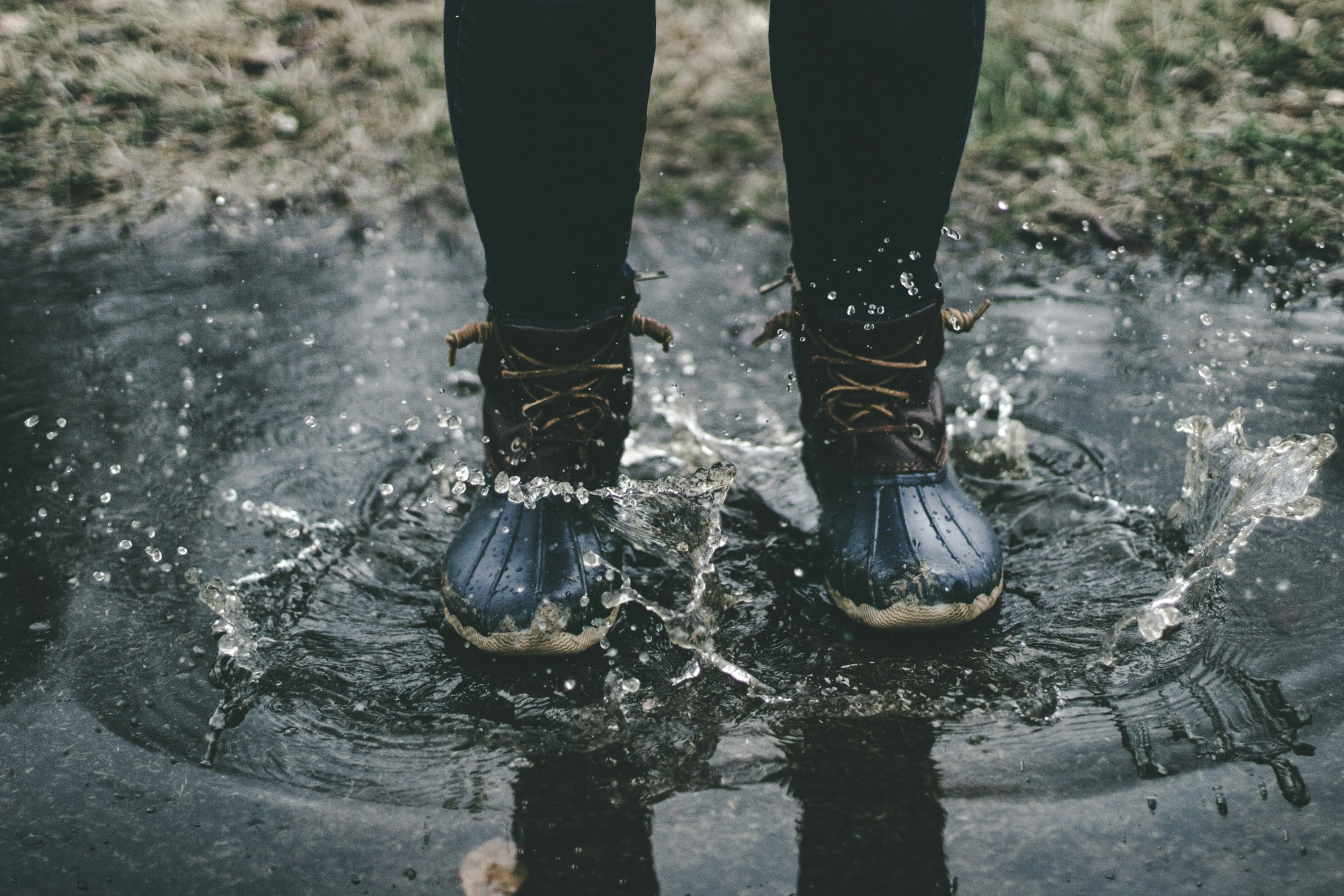 A person splashing into a puddle of water. It is a close up of their black boots.