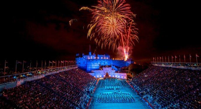 An aerial view of Edinburgh Castle. The castle is bathed in blue light, there are fireworks overhead. 