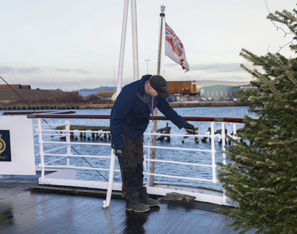 A Maintenance man is on the Verandah Deck painting the railings white. The Port of Leith is in the background. 