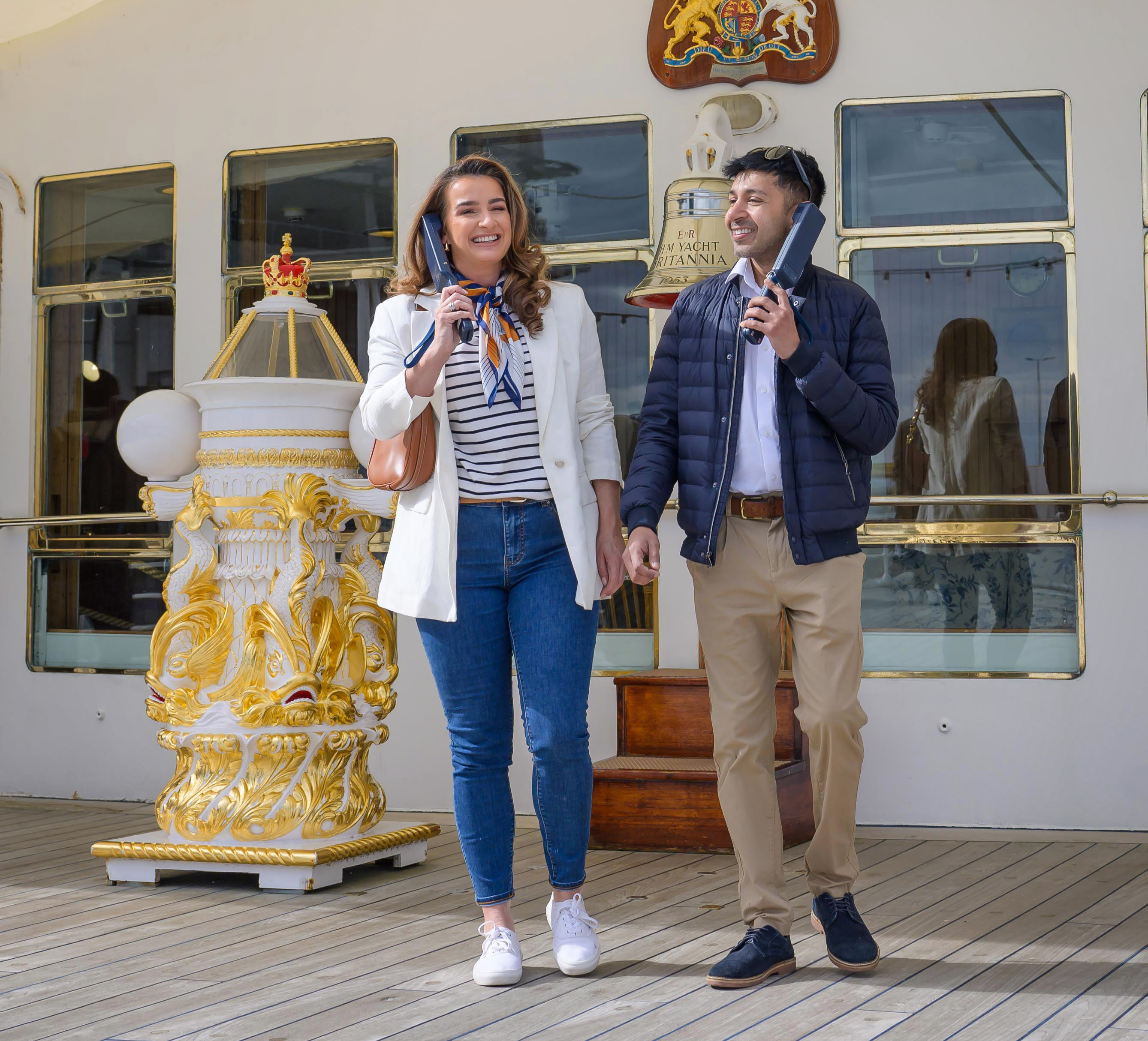 A man and woman are listening to audio guide handsets on Britannia's Verandah Deck in the Port of Leith.