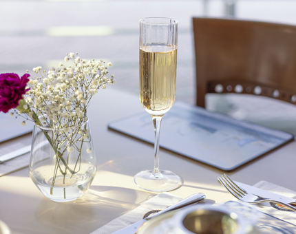 A glass of Champagne is on a table with a small vase of flowers. 