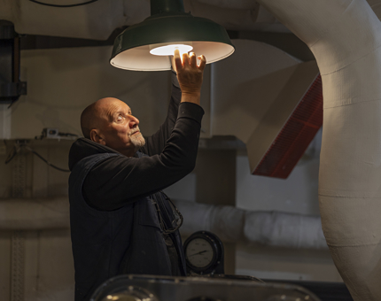 A maintenance team member reaching up to change a lightbulb. The light is on. 