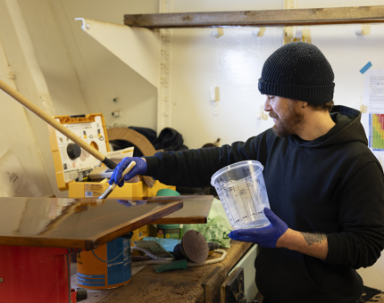 A Maintenance man is varnishing a wood panel. 