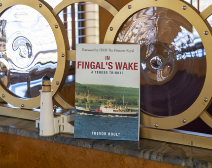 A book, In Fingal's Wake, is sitting on a ledge next to a model of a lighthouse. 