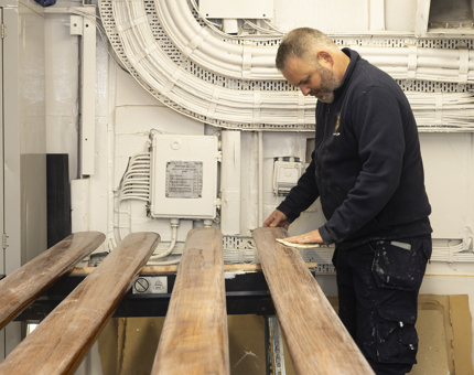 A Maintenance man is sanding wooden handrails. 