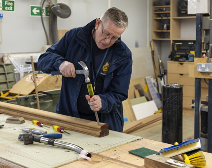 A Maintenance man is using a hammer and chisel to work on a wooden handrail. 