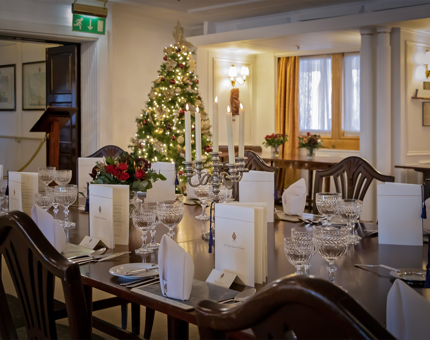 The State Dining Room with the tables set and a lit up Christmas tree in the corner. 